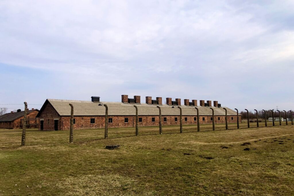 Obraz przedstawia budynek z cegiel w pobliżu szpagi, który przypomina komórkę z obozu koncentracyjnego Auschwitz. Jest to miejscówka o dużej wartości historycznej i symbolicznej. Gdy chodzi o skuteczne promowanie marki na Facebooku, takie miejsca mogą być inspiracją dla treści związanych z historią, edukacją czy wartościami. Można tworzyć posty, które będą związane z tą miejscówką, na przykład opowiadać historię obozu, wskazywać na ważność pamięci historycznej, a w ten sposób związać markę z tematykiem, która wzbudza emocje i zainteresowanie odbiorców.